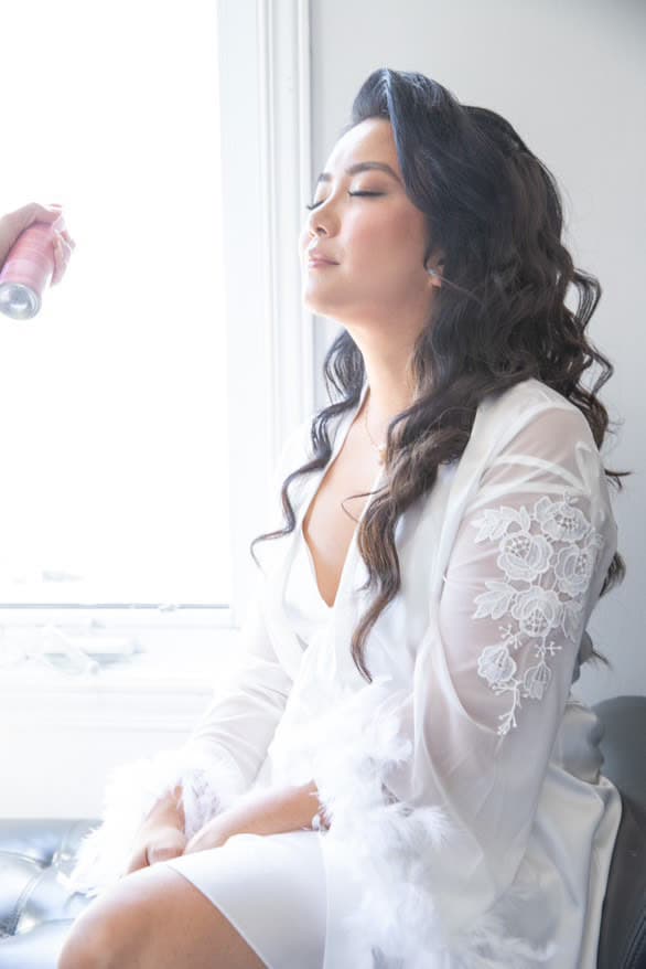 Bride in a lace robe during the morning preparations, hair finished, setting spray being applied