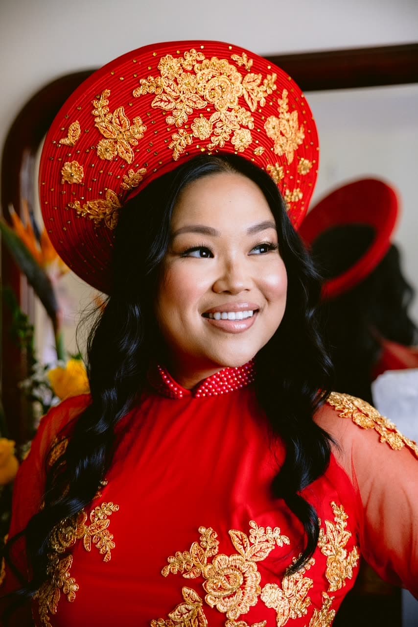 Portrait de mariée en áo dài rouge et coiffe traditionnelle dorée, teint lumineux