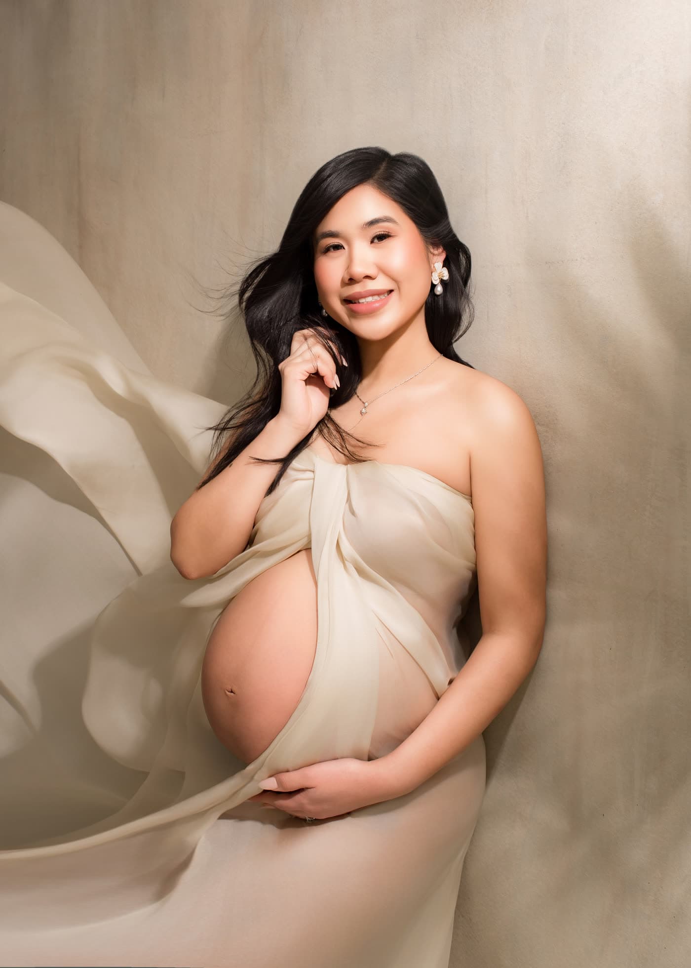 Maternity portrait: ivory silk drape, luminous skin and a nude lip, in studio